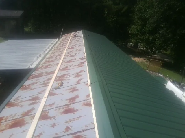 Old rusted panels beside newly installed green metal roofing — Wind Damage Roof Repair by Roofing Brothers in Plains