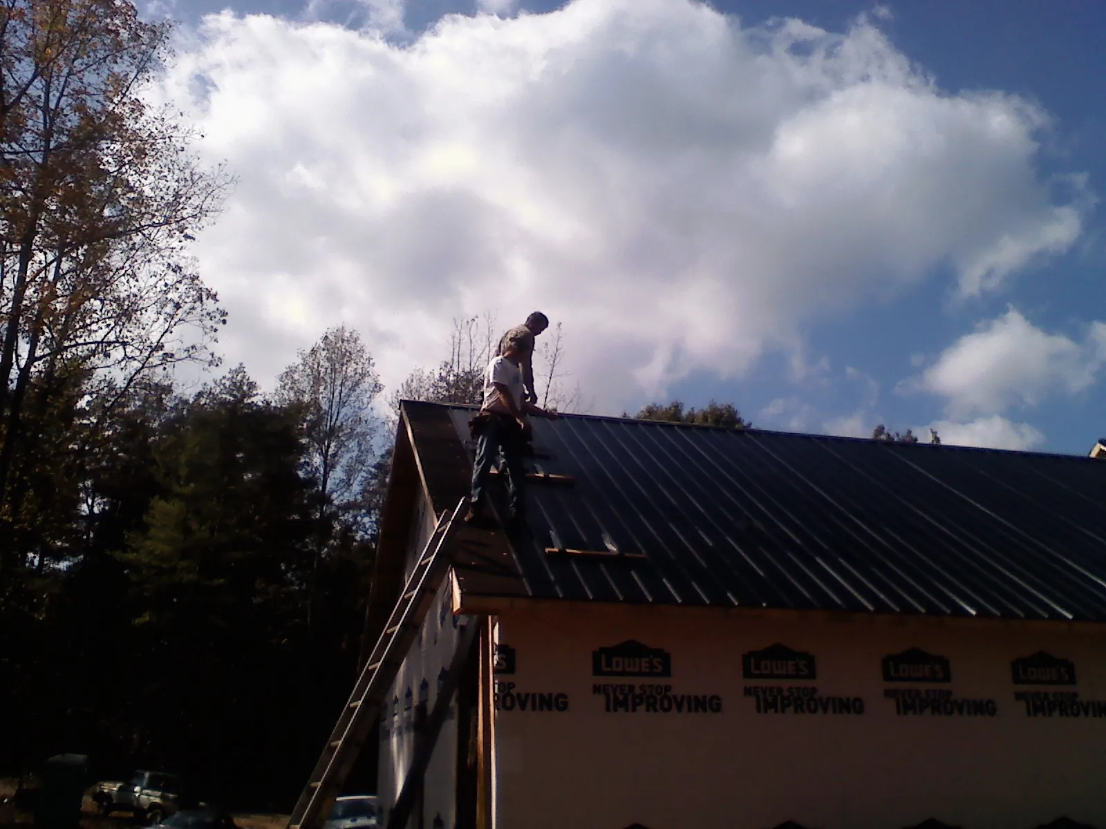 Roofer fastening dark metal panels high against a cloudy sky, from a Roof Inspection job in Plains