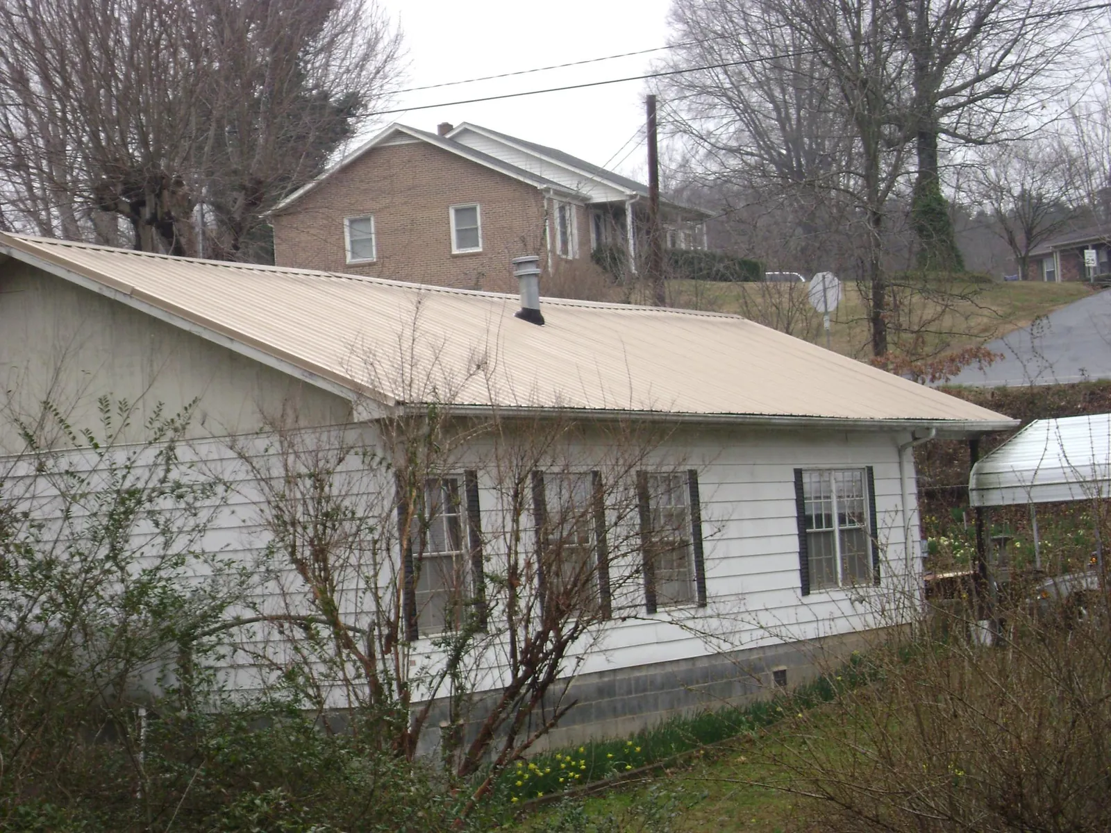 Tan metal roof on a white sided house set into a hillside — Commercial Roofing by Roofing Brothers in Plains