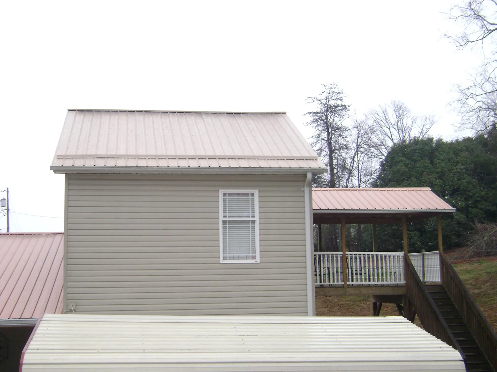 Tan metal roofs on a two story addition and attached porch, from a Roof Replacement job in Plains